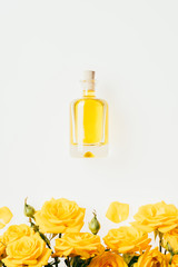 top view of bottle of perfume and yellow roses on white