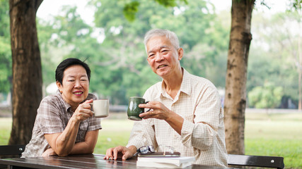 Asian senior couple relax drinking coffee in summer park, green nature