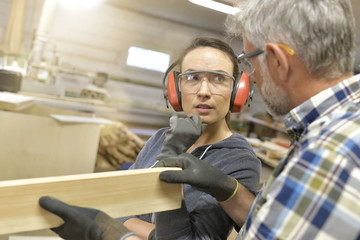 Carpenter teaching apprentice how to cut wood