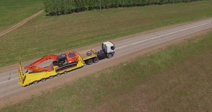 Orange digger travelling on truck with long trailer - Aerial View
