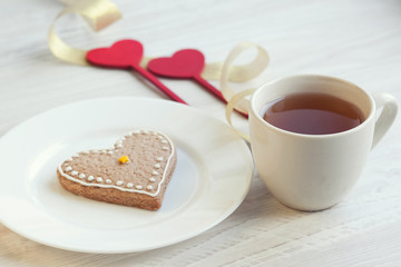 Love consept.  Valentines day. Gingerbread in the shape of heart, a cup of tea, decorative hearts on a wooden table 