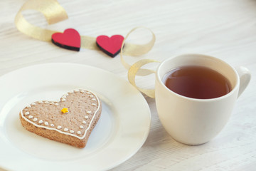 Love consept.  Valentines day. Gingerbread in the shape of heart, a cup of tea, decorative hearts on a wooden table 