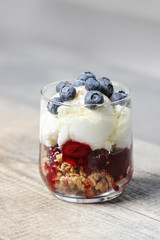 Layer strawberry, blueberry and muesli dessert in transparent glass goblet.