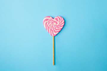 a pink and white spiral heart lollipop on blue background, flat lay minimal concept, trendy pop art...