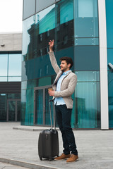 Be successful! Smiling handsome young man having come after business trip, drinking his coffee and waving down the taxi in order to get his office.