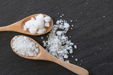 White salt in wooden spoon with black background.