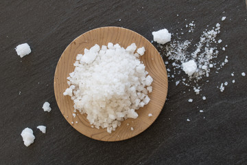 White salt in wooden dish with black background.