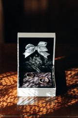 Two luxury wedding rings in stylish box with a white ribbon on a wooden table, couple of golden wedding rings in a case
