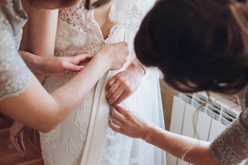 Beautiful bridesmaids help put on wedding dress on gorgeous blonde bride in luxury hotel room...