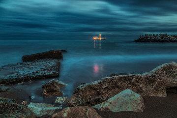 The night shore of the sea with the ship in the distance.