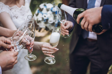 happy group of people toasting with champagne. man holding bottle of champagne and pouring drink into glasses. bride bridesmaids and groom groomsmen having fun. holiday celebration