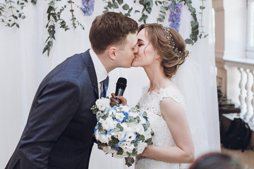 bride with microphone kissing with groom after toast at wedding reception. luxury decorated wedding centerpiece with purple flowers