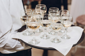glasses of champagne or wine on tray. waiter serving champagne at wedding reception in restaurant. luxury catering. christmas celebration, drinks at feast
