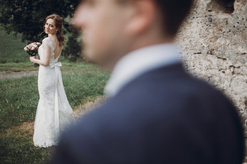 Naklejka premium Gorgeous romantic bride in elegant wedding dress looking at groom outdoors, beautiful newlywed bride giving a sensual look to camera, love concept