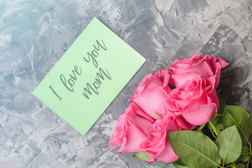 Pink roses and a green card with the inscription I love you mom on a gray concrete background