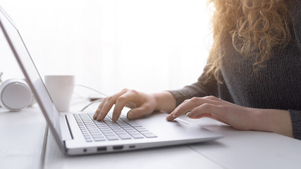 Woman sitting at desk and connecting with her laptop, she is working and typing on the keyboard,...