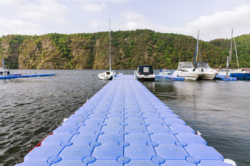 Plastic pontoon pier leading to to anchored yachts and sailing boats. © murmakova