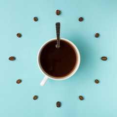 Coffee cup and roasted beans arranged as clock face on blue background, top view. Coffee time symbol. Interesting idea energy and refreshment concept.