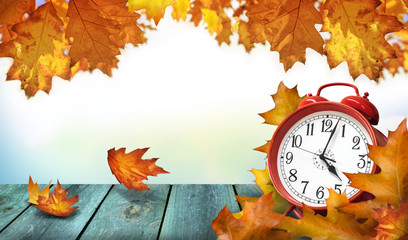 Clock and autumn leaves on wooden table - daylight saving time concept