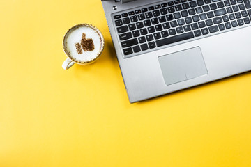 A cup of cappuccino on which is drawn a smile like a thumb up. Next to the laptop. Communication in...