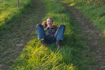 Naklejka na ściany i meble Happy teenage man having fun with dog in countryside during spring.