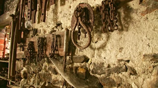 In an old workshop, blacksmith tools are on the wall. Cobwebs and lime plaster remnants accumulate on the tools. Much time has passed in this deserted place.