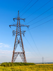 High voltage electricity pole and transmission power lines on the blue sky background.