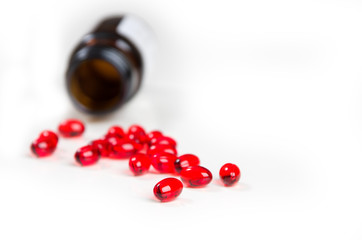 Tablets of red color vitamin E and bottle on a white background.