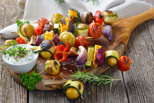 Vegan grillen: Bunte  Gemüsespieße vom Grill mit Kräuterdip  - Grilled skewers with mixed vegetables served  on a wooden cutting board with a vegan herb dip