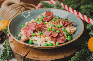 Top view russian traditional salad Olivier with vegetables and meat. Salad on a plate on a on wooden board, orange mandarin, candy sticks, christmas tree background. New year food theme.