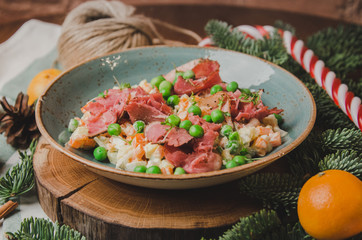 Top view russian traditional salad Olivier with vegetables and meat. Salad on a plate on a on wooden board, orange mandarin, candy sticks, christmas tree background. New year food theme.