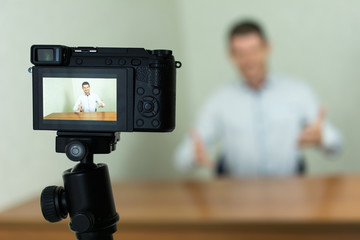 Young male blogger recording video at home using a tripod mounted digital camera