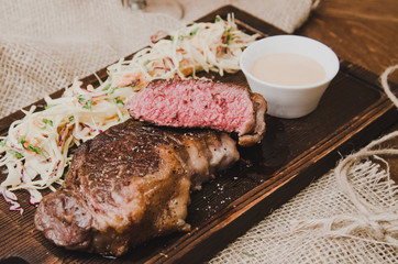 Sliced grilled ribeye beef steak with stew cabbage and wineglass of red wine, herbs and spices over brown sackcloth on wooden table,brown brick wall background.