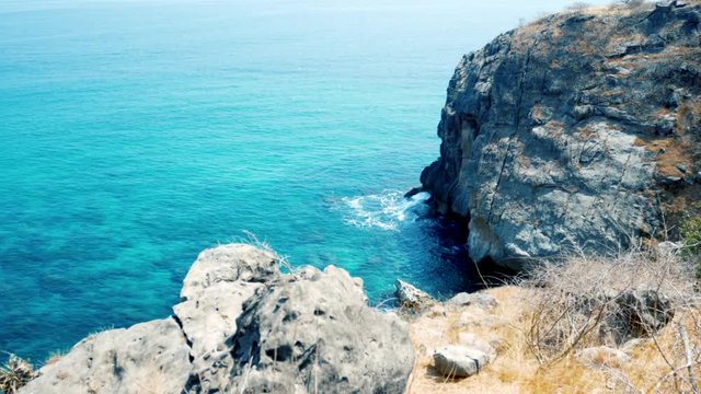 Looking from the cliffs above as gentile ocean waves lap against the rocky cliffs below