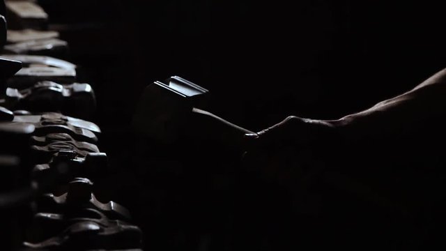 Close-up of a man's hand throws a hammer and rotates it on a dark background in the contour light. Brutal powerful concept