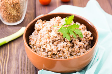Cooked buckwheat in a bowl with a leaf of parsley and cherry tomatoes on a wooden table