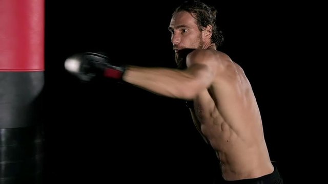 Slow motion of boxer punch a punching bag. Young white man with beard in black background. Fighting sport fitness concept.