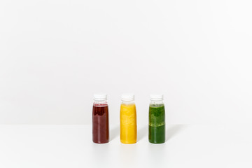 Green, red and yellow detox smoothies in bottles on table isolated on white background. Proper nutrition, vegetarian drink, healthy lifestyle, dieting concept. Big advertising area with copy space.
