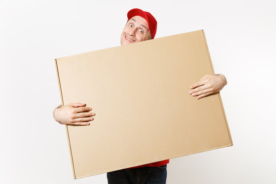 Delivery man in red uniform isolated on white background. Male in cap, t-shirt, jeans working as courier or dealer holding big large heavy empty blank cardboard box. Receiving package. Copy space area