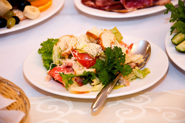 Salad with tomatoes, chicken, croutons and greens in a white plate with a spoon, on a табл.