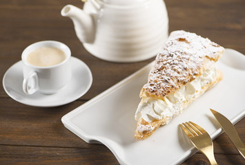 Close-up of delicious breakfast of coffee with sweet puff pastry with cream on brown wooden table. Horizontal shoot. Food