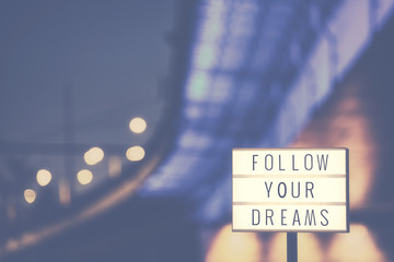 Follow Your Dreams inspirational life quote text in lightbox, city lights in background, color...