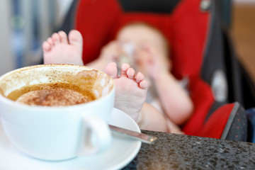 Cup of coffee and baby on background. Concept of working mother and newborn baby