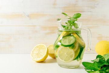 Detox water infused with sliced lemon, cucumber and sprigs of mint on wooden background.