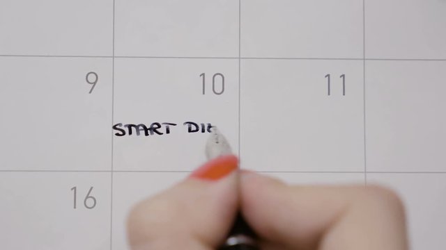 Top view of woman hands writing start diet again with capital letters in calendar and then doddle it using a black pen