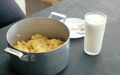Making mashed potato in saucepan. Glass of milk on the table.