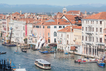 View of the Grand Canal with sailing ships, houses with red roofs and mountains in the distance, a bright sunny day in Venice, Italy.