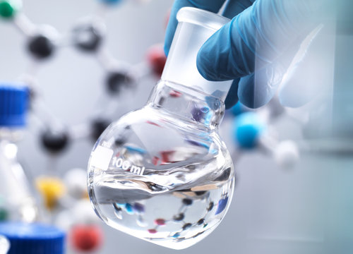 Scientist preparing chemical formula in a laboratory flask during an experiment, molecular model in the background