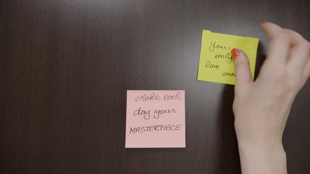 Top view of female hands sticking handwritten post it notes that contains motivational quotes on her dark wooden desk at work