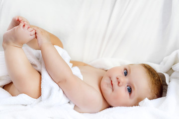 Cute little baby playing with own feet after taking bath. Adorable beautiful girl wrapped in white towels